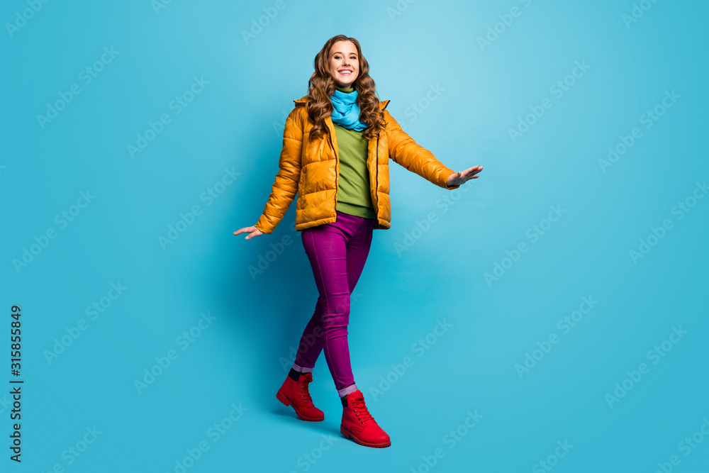Full body photo of pretty lady traveler walking down street abroad good mood wear yellow overcoat scarf violet trousers green jumper red shoes isolated blue color background Full body photo of pretty lady traveler walking down street abroad good mood wear yellow overcoat scarf violet trousers green jumper red shoes isolated blue color background