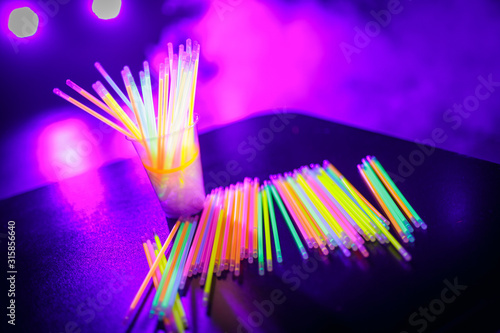 Multicolored UV fluorescent sticks in a glass at a techno party