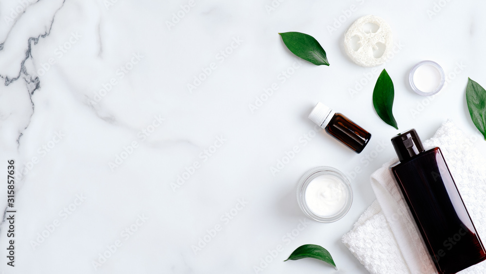 Natural organic cosmetic products and green leaves on marble background. Minimal flat lay style composition with essential oils, shampoo bottle, towel, hand cream. Body care, skincare concept - obrazy, fototapety, plakaty 