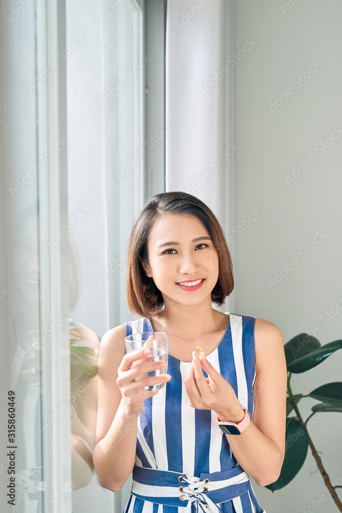 Portrait of beautiful Asian woman holding water glass and medicine / vitamin to drink Portrait of beautiful Asian woman holding water glass and medicine / vitamin to drink