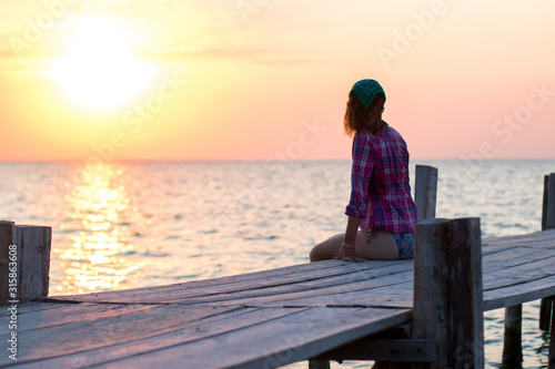 the girl is sitting on the old wooden berth and admires sunset at sea
