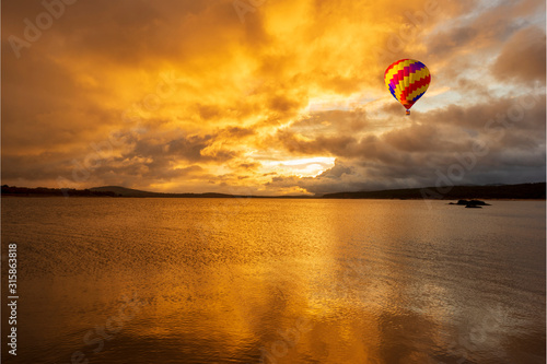 A balloon flying over a lake in a beautiful sunrise