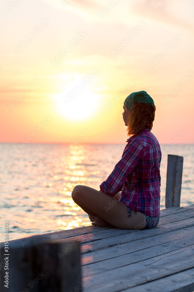 girl doing yoga asana on an old wooden pier and enjoys the sunset on the sea