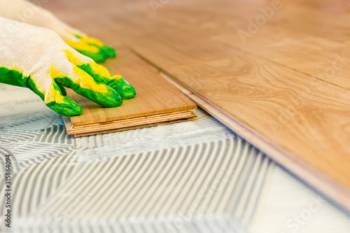 The master smears the glue on the concrete floor and carefully lays the parquet. Professional parquet laying.