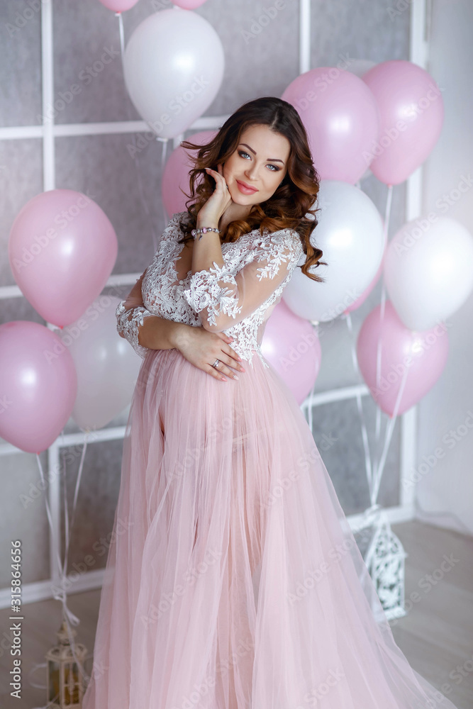 Pregnant bride with long hair on a background of pink-white balloons.