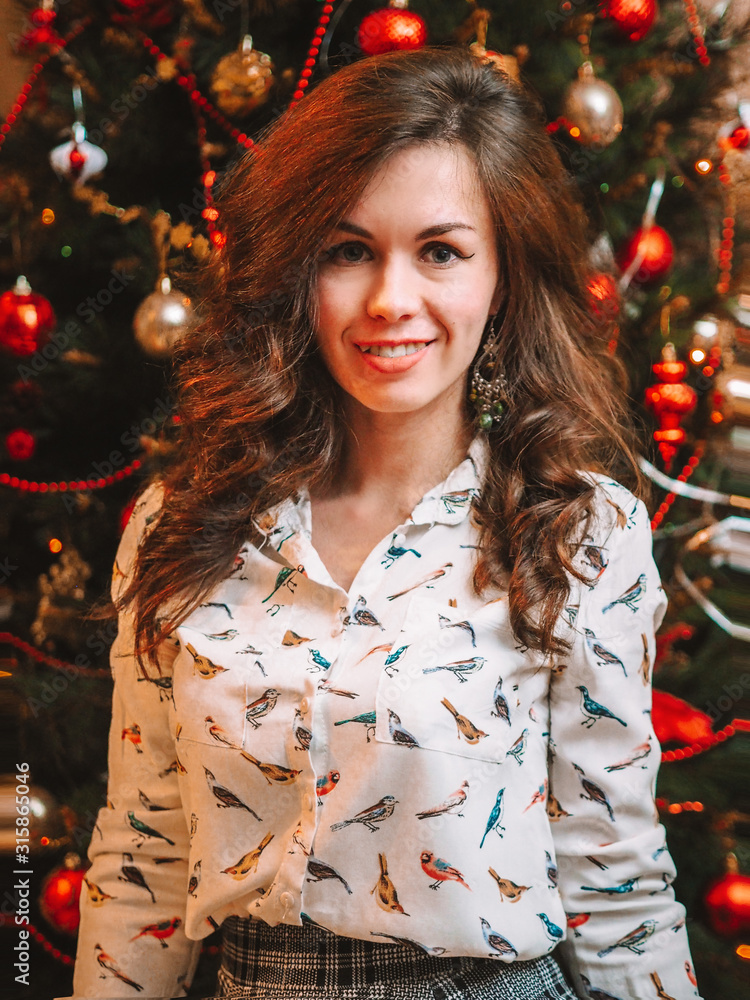 A brunette girl with a chic shock of hair in a skirt and a white shirt stands near a Christmas tree decorated with Christmas atmosphere A brunette girl with a chic shock of hair in a skirt and a white shirt stands near a Christmas tree decorated with Christmas atmosphere