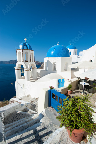 Bright scenic view of the Mediterranean hillside village of Oia in Santorini, Greece with gate matching sky blue Greek church domes 