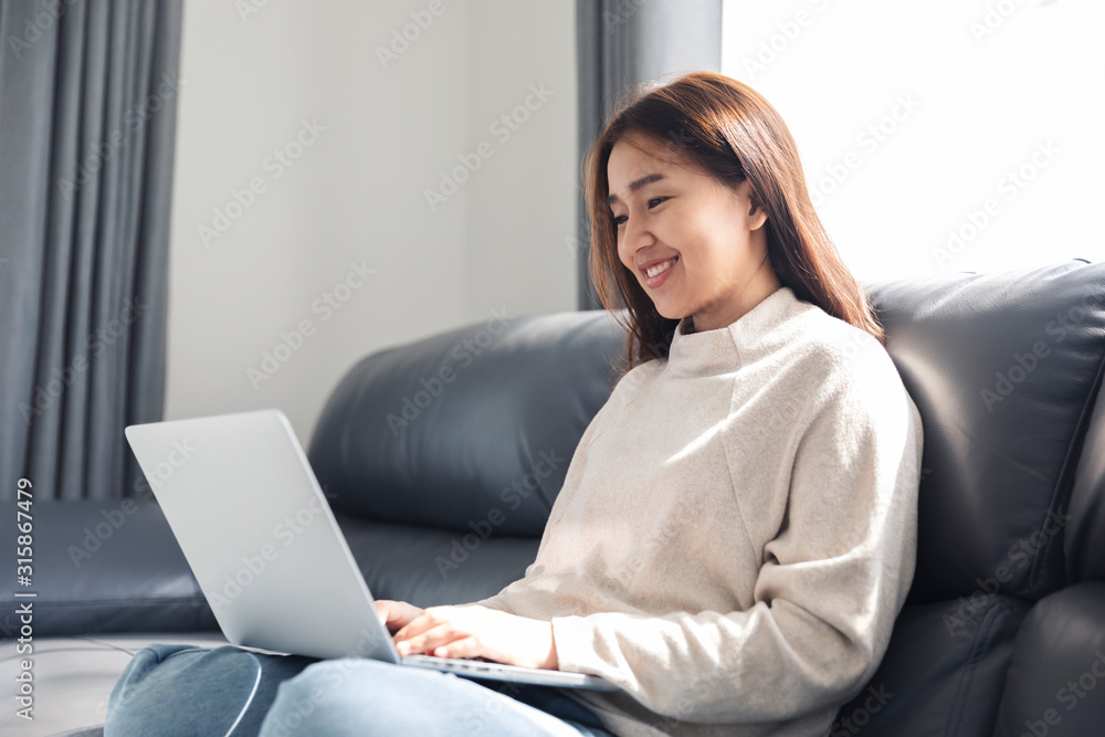 Young woman doing research work for her business, Smiling woman sitting on sofa relaxing while browsing online shopping website Young woman doing research work for her business, Smiling woman sitting on sofa relaxing while browsing online shopping website