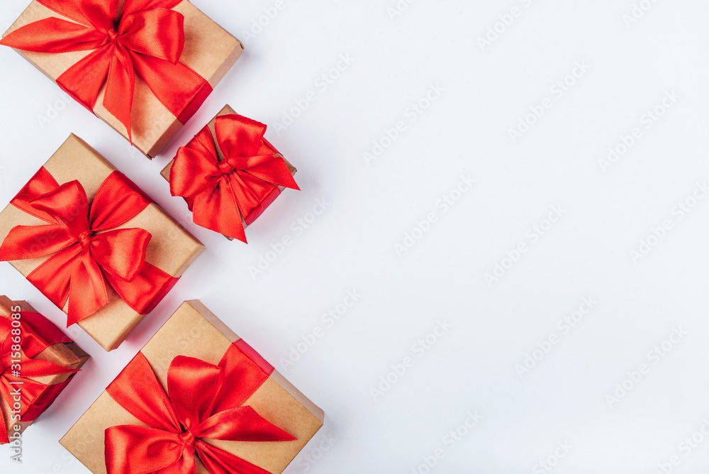 Frame of cardboard gift boxes with red bows on white background. Flat lay, top view. Copy space for text.