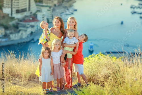 A large family of relatives together two mothers and five children stand on the top of the mountain above the water. © ElenaBatkova