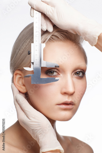 fashionable blonde female face isolated on white background, doctor's hands wearing latex gloves measuring idylic propotions of her face, beauty concept. photo