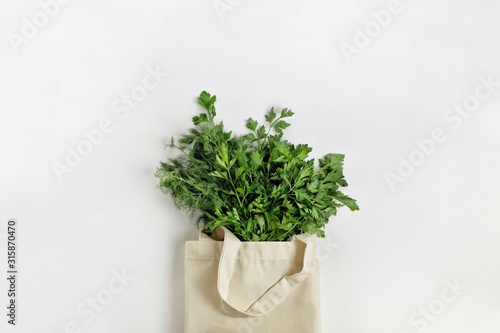 A bunch of fresh organic greenery parsley and dill in a cotton reusable bag on a white background. Healthy food, organic products, eco friendly lifestyle, zero waste concept. Top view, copy space.