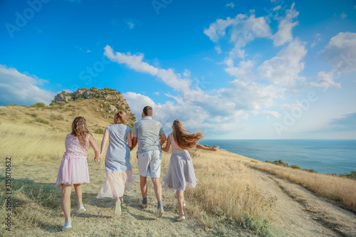 A full family of four mom dad and two daughters all together on a mountaintop above the sea.
