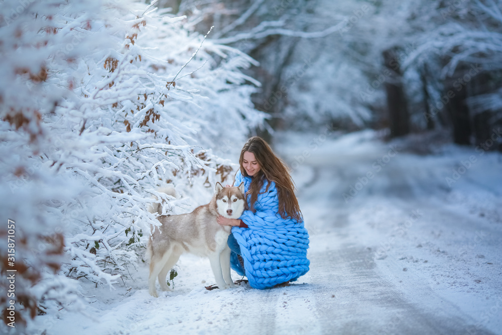 A young woman with a husky dog squats along a snowy road. A young woman with a husky dog squats along a snowy road.