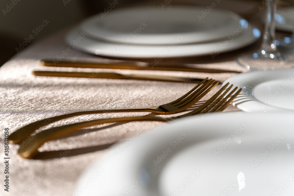Chic and elegant, gold-plated cutlery and white plates, table setting with empty plates. Macro. Chic and elegant, gold-plated cutlery and white plates, table setting with empty plates. Macro.
