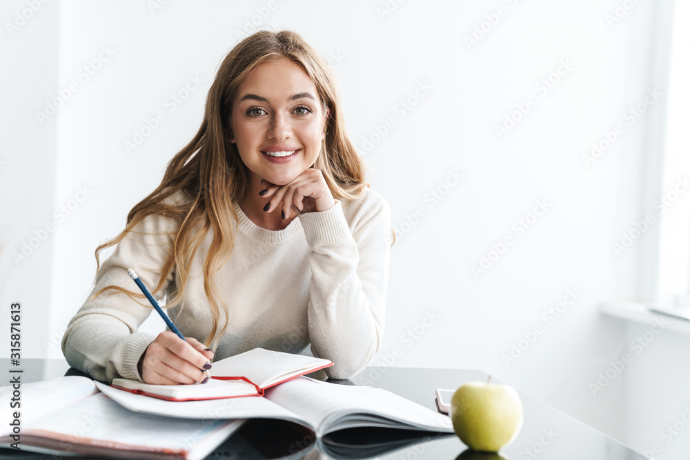 Photo of young happy woman smiling and making notes in exercise book Photo of young happy woman smiling and making notes in exercise book