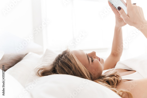 Photo of joyful caucasian woman smiling and using cellphone while lying