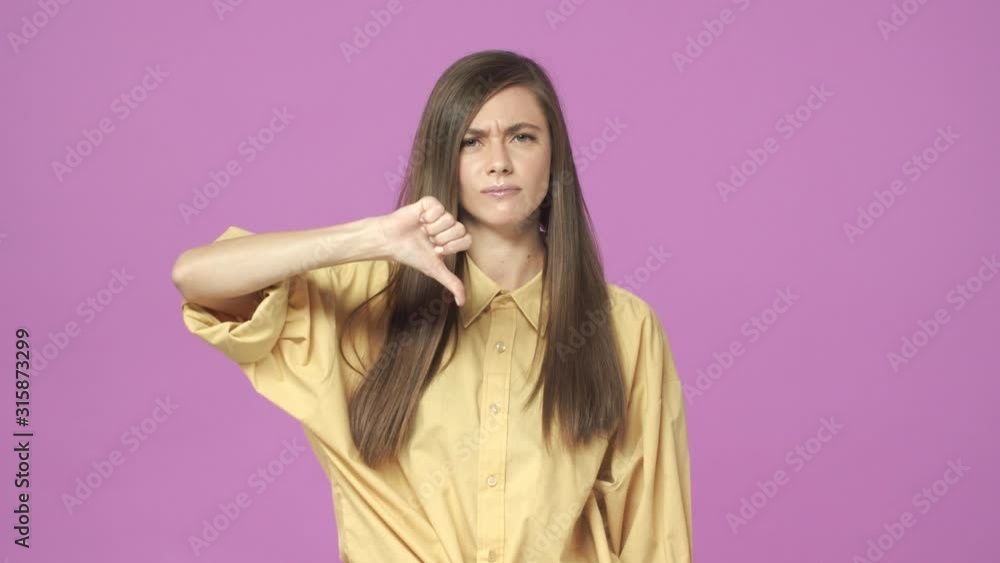 Very bad. Slow-motion displeased, angry and unsatisfied young modern woman in shirt, strongly disagree, showing thumb-down, frowning and pouting upset with awful situation, purple background Very bad. Slow-motion displeased, angry and unsatisfied young modern woman in shirt, strongly disagree, showing thumb-down, frowning and pouting upset with awful situation, purple background