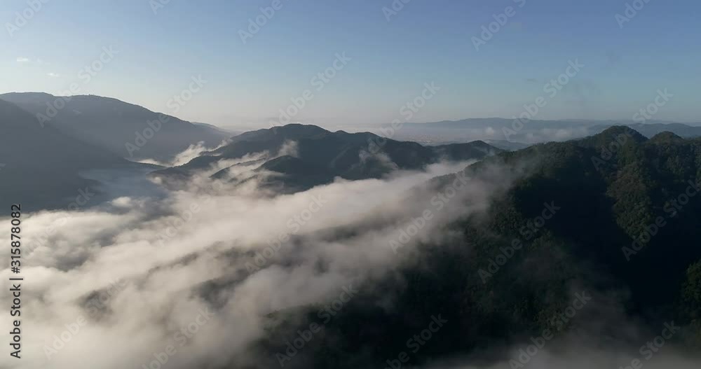 Mountain ranges and valley around greater Kyoto city in Japan in elevated aerial hovering in soft morning light. Mist and clouds rising above valleys between forest mountains. Mountain ranges and valley around greater Kyoto city in Japan in elevated aerial hovering in soft morning light. Mist and clouds rising above valleys between forest mountains.