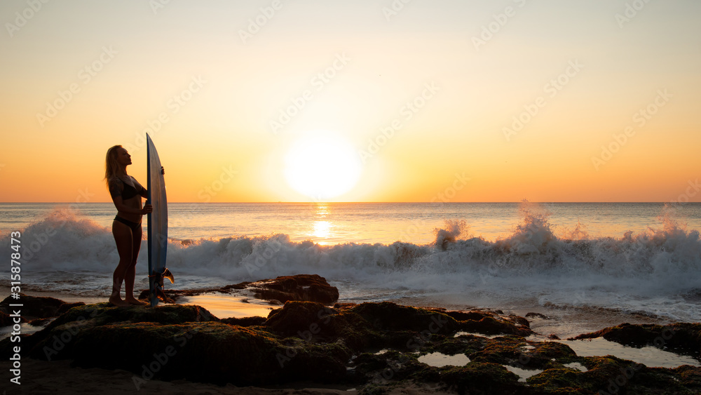 Silhouette of surfer girl with surfboard on the beach. Golden sunset time. Bali, Indonesia