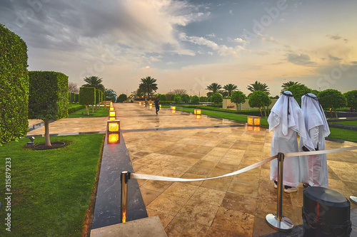 Two arab men in a traditional white clothes standing in the green park of Abu Dhabi at dusk