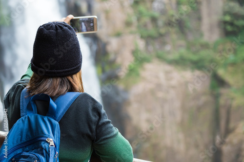 Woman taking photo waterfall in forest by smartphone