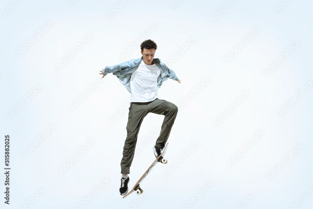 Caucasian young skateboarder riding isolated on a white studio background. Man in casual clothing training, jumping, practicing in motion. Concept of hobby, healthy lifestyle, youth, action, movement.