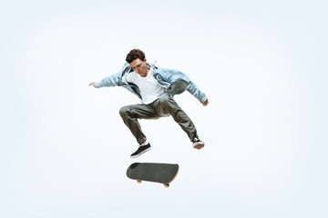 Caucasian young skateboarder riding isolated on a white studio background. Man in casual clothing training, jumping, practicing in motion. Concept of hobby, healthy lifestyle, youth, action, movement.