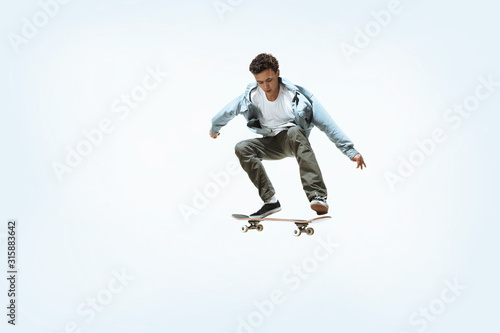 Caucasian young skateboarder riding isolated on a white studio background. Man in casual clothing training, jumping, practicing in motion. Concept of hobby, healthy lifestyle, youth, action, movement.