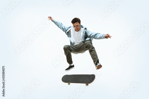 Caucasian young skateboarder riding isolated on a white studio background. Man in casual clothing training, jumping, practicing in motion. Concept of hobby, healthy lifestyle, youth, action, movement. photo