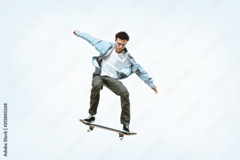 Caucasian young skateboarder riding isolated on a white studio background. Man in casual clothing training, jumping, practicing in motion. Concept of hobby, healthy lifestyle, youth, action, movement.