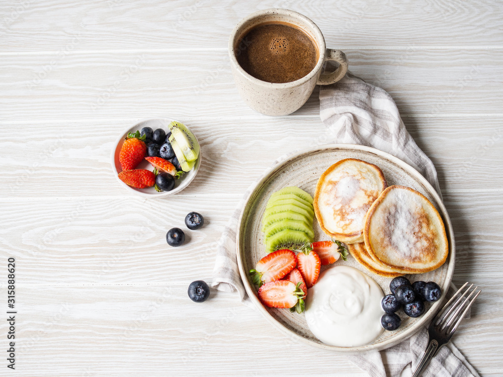 Delicious breakfast - fritters pancakes, sprinkled with powdered sugar with fruits and berries Delicious breakfast - fritters pancakes, sprinkled with powdered sugar with fruits and berries