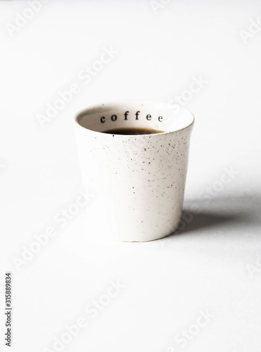 White ceramic cup of black coffee on white background. Copy space