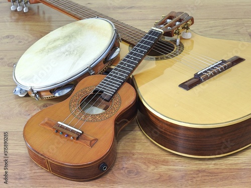 An acoustic guitar and two Brazilian musical instruments: cavaquinho and pandeiro (tambourine), on a wooden surface. The instruments are widely used to accompany samba and choro music. photo