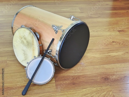 Three Brazilian percussion musical instruments: “tantan” (or “rebolo”), pandeiro (tambourine) and tamborim with drumstick, on a wooden surface. They are widely used in samba and pagode ensembles.