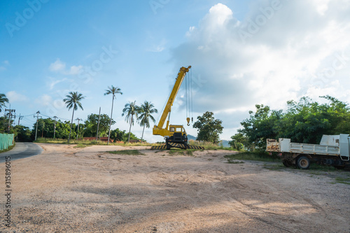 Yellow automobile crane with risen telescopic boom outdoors. Mobile construction crane on a constructin site. Crane machine stand by waiting for work under the construction building. Heavy industry. photo