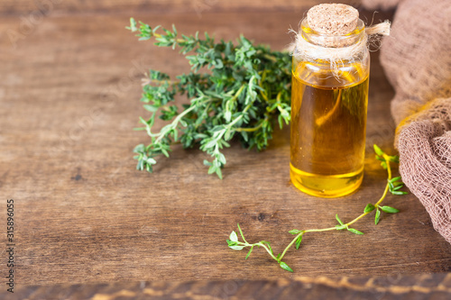 Bottle of thyme (thymus) essential oil with fresh thyme, old wooden background.