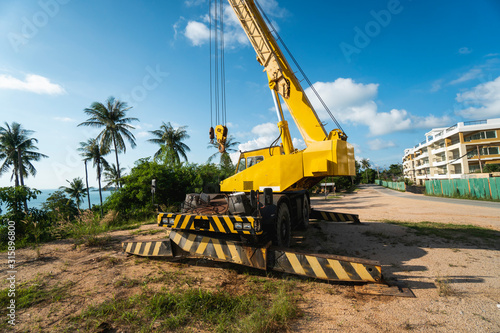 Yellow automobile crane with risen telescopic boom outdoors. Mobile construction crane on a constructin site. Crane machine stand by waiting for work under the construction building. Heavy industry.