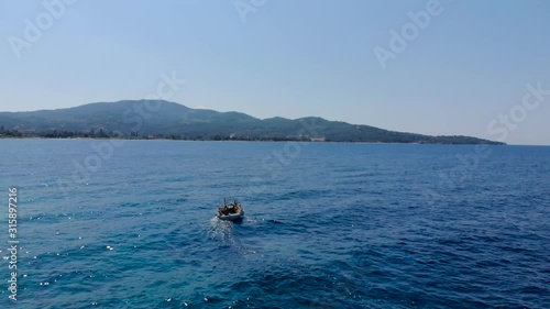 Drone aerial shot of small wooden fishing boat in crystal clear blue waters of Greece coastline.