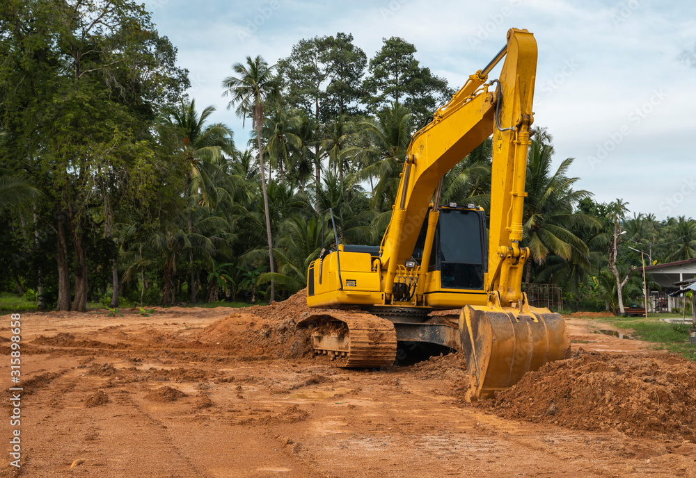 Yellow excavator on a construction site against blue sky. Heavy industry. Close up details of industrial excavator. Large tracked excavator standing on a orange ground with a palms on background.