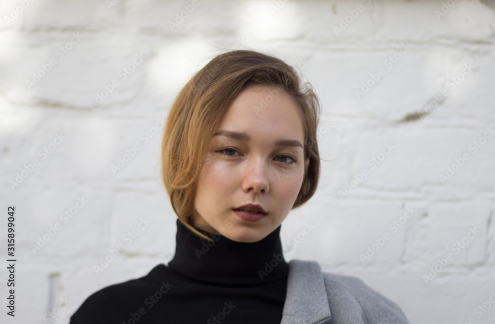 Portrait of young caucasian woman looking at camera with calm look on the white brick background Portrait of young caucasian woman looking at camera with calm look on the white brick background