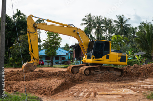 Yellow excavator on a construction site against blue sky. Heavy industry. Close up details of industrial excavator. Large tracked excavator standing on a orange ground with a palms on background.