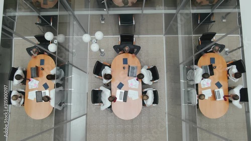 Top view. Colleagues office workers enter office space meeting room and sit at the table. Business partners come and prepare for negotiations and presentations on flipchart