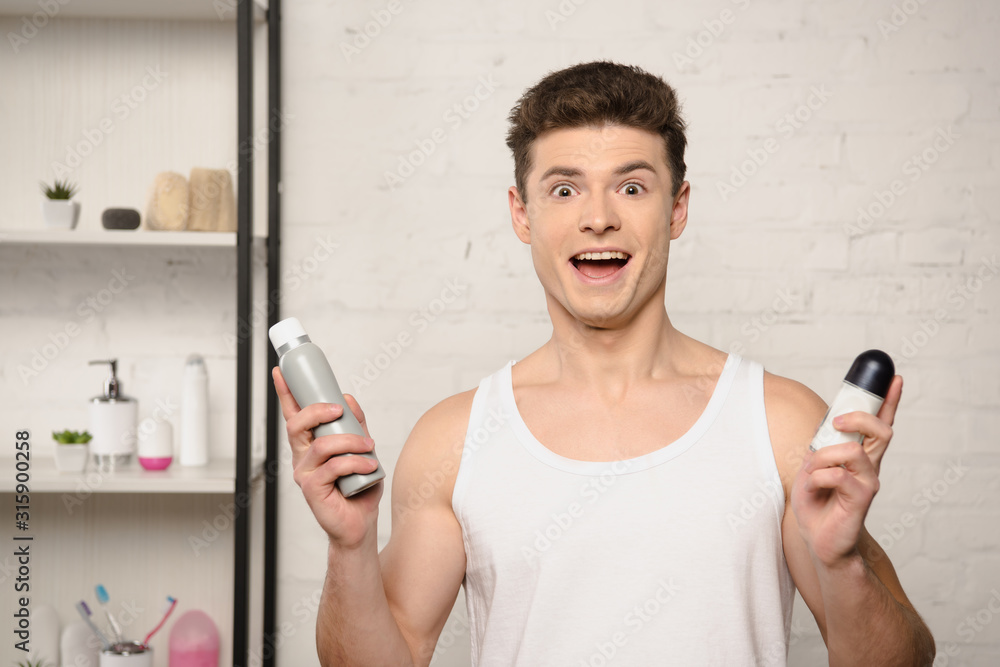 excited young man in white sleeveless shirt looking at camera while holding deodorants excited young man in white sleeveless shirt looking at camera while holding deodorants