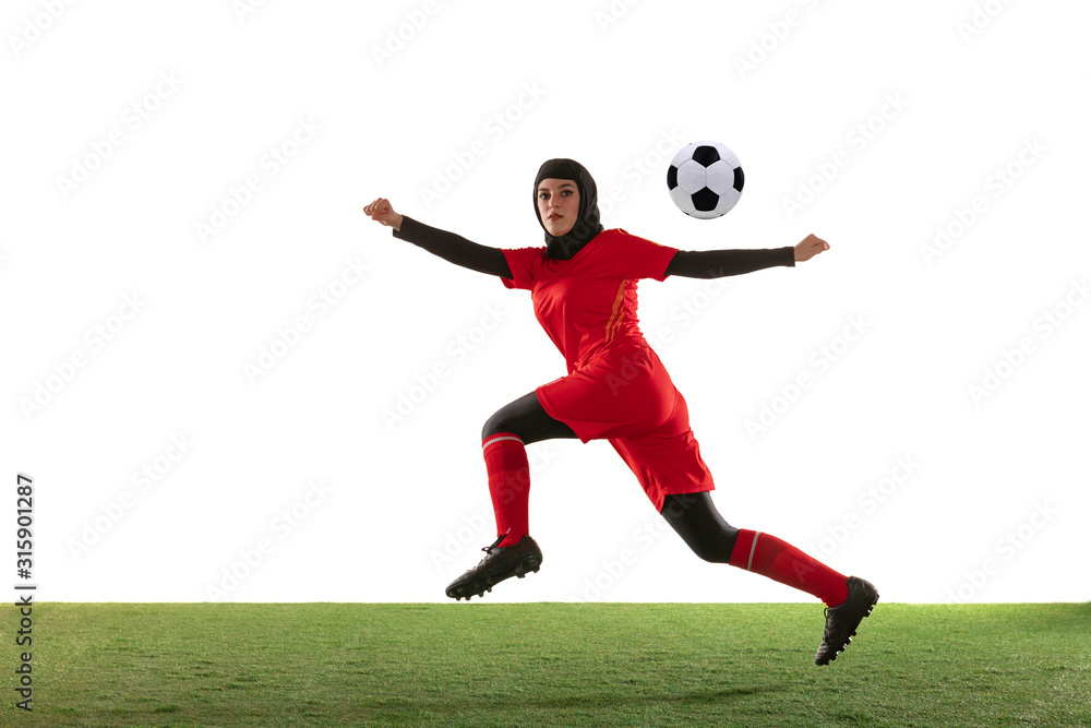 Arabian female soccer or football player isolated on white studio background. Young woman kicking the ball, training, practicing in motion and action. Concept of sport, hobby, healthy lifestyle.
