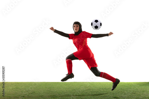 Arabian female soccer or football player isolated on white studio background. Young woman kicking the ball, training, practicing in motion and action. Concept of sport, hobby, healthy lifestyle. © master1305