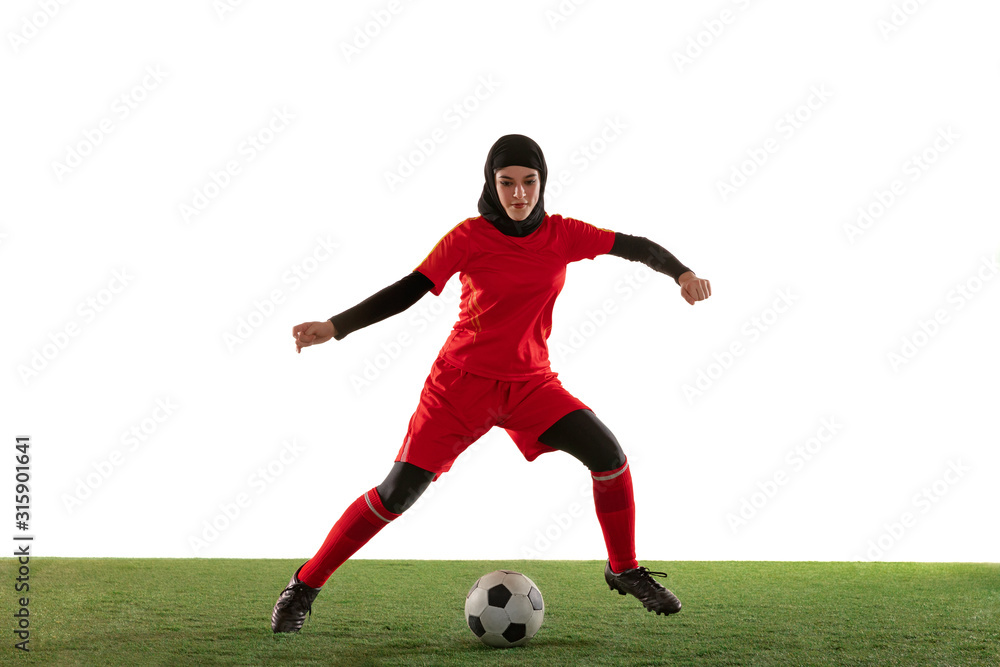 Arabian female soccer or football player isolated on white studio background. Young woman kicking the ball, training, practicing in motion and action. Concept of sport, hobby, healthy lifestyle. Arabian female soccer or football player isolated on white studio background. Young woman kicking the ball, training, practicing in motion and action. Concept of sport, hobby, healthy lifestyle.