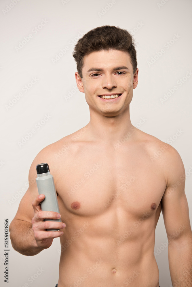 Fototapeta premium smiling shirtless man looking at camera while holding deodorant isolated on grey