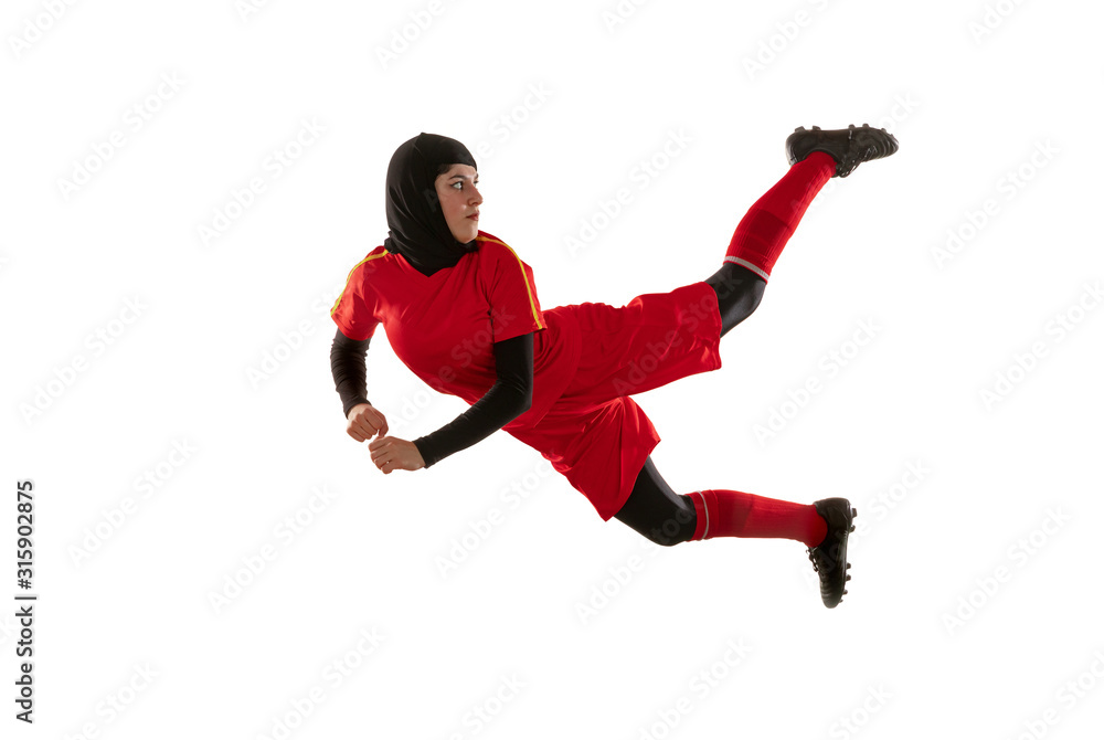 Arabian female soccer or football player isolated on white studio background. Young woman kicking ball in jump, catched in air, training in motion, action. Concept of sport, hobby, healthy lifestyle.