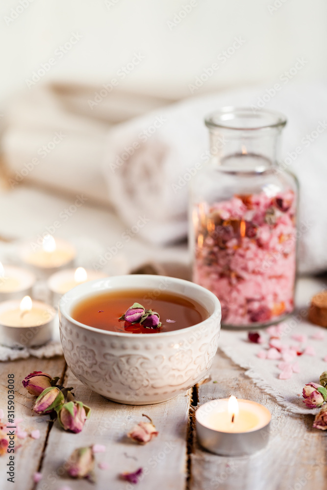 Concept of spa treatment with roses. Herbal tea, crystals of sea pink salt in bottle, candles as decor. Atmosphere of relax, anti-stress and detox procedure. Luxury lifestyle. Wooden background Concept of spa treatment with roses. Herbal tea, crystals of sea pink salt in bottle, candles as decor. Atmosphere of relax, anti-stress and detox procedure. Luxury lifestyle. Wooden background